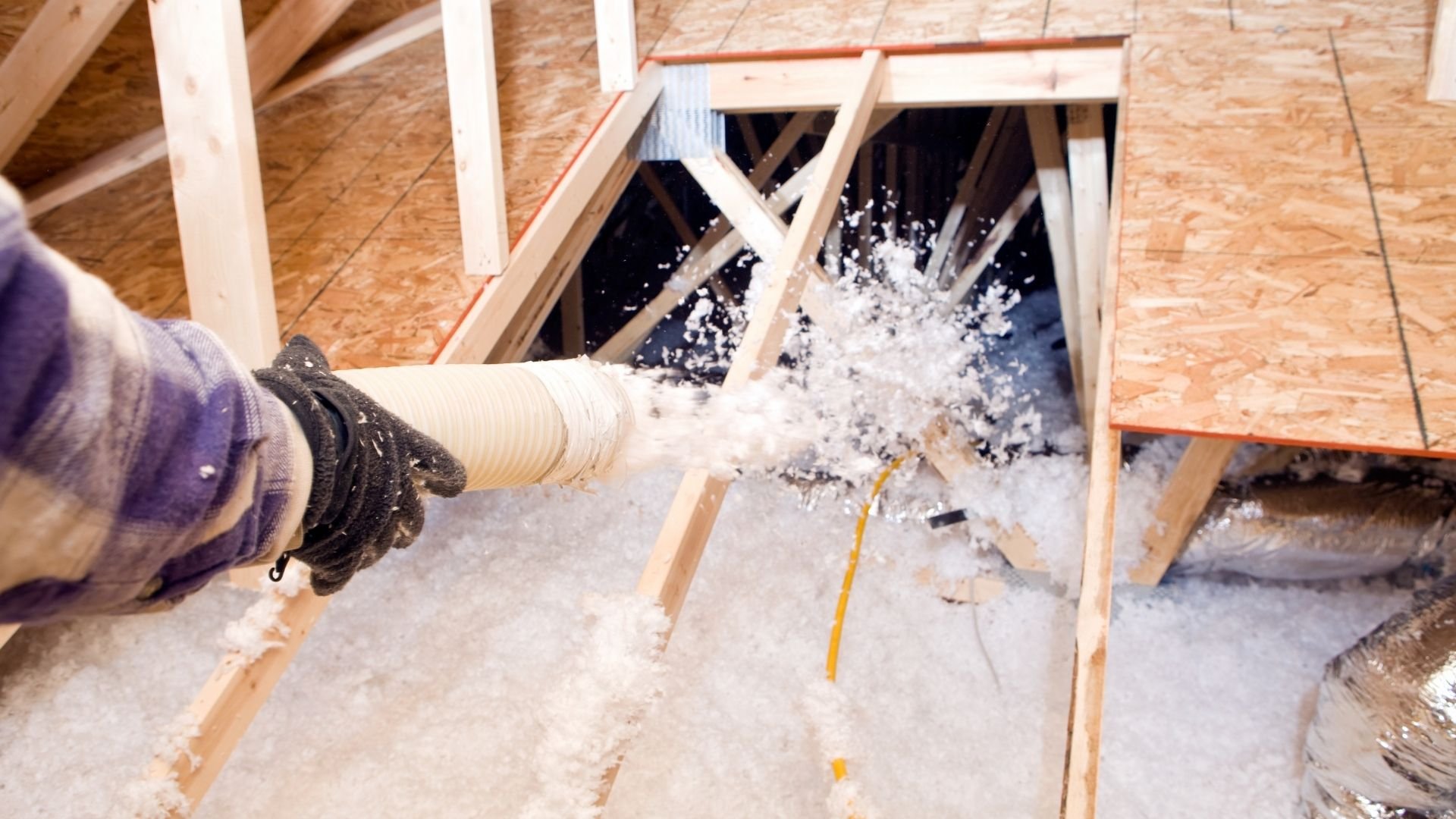 Worker blowing insulation into attic space through flexible duct during home construction