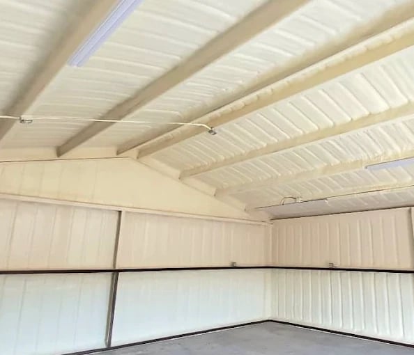 Empty metal warehouse interior with white corrugated walls and beamed ceiling