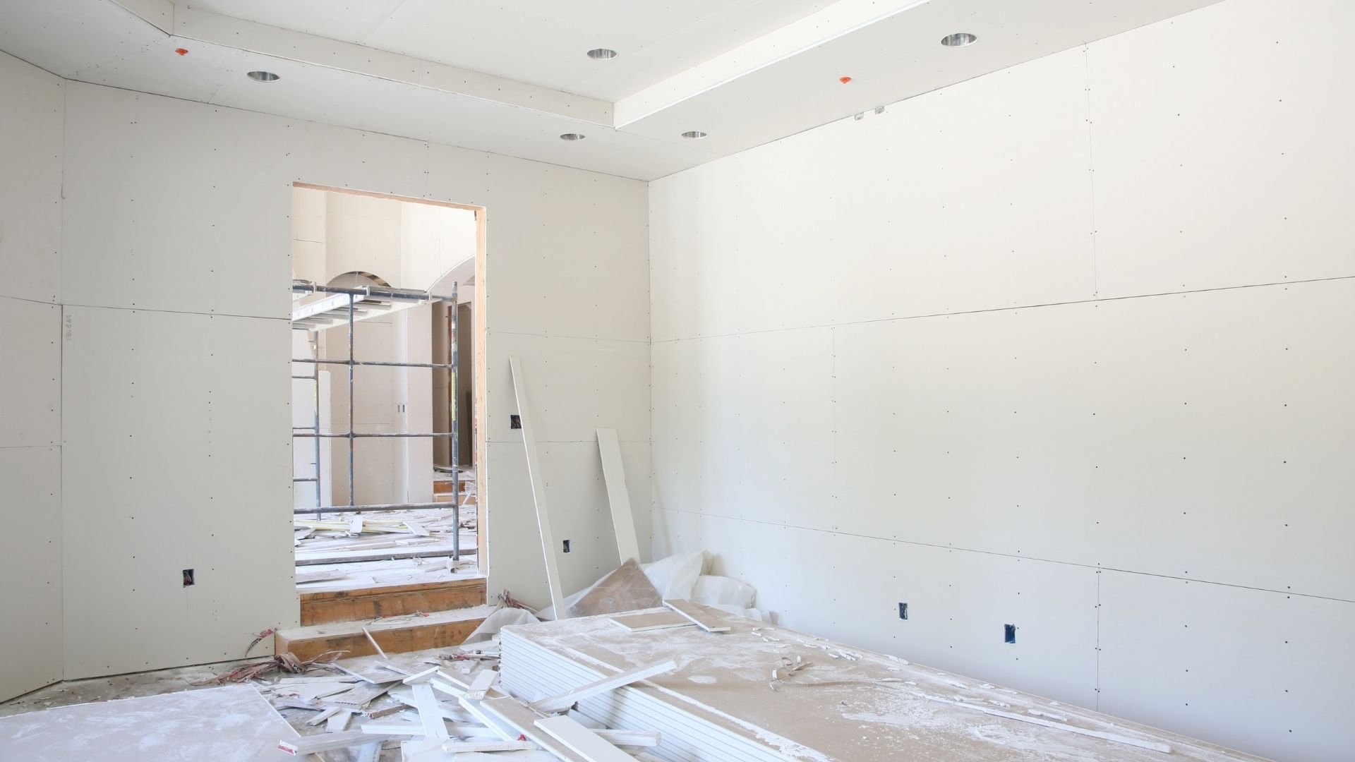 Construction site with drywall sheets, debris, and unfinished white walls and ceiling.