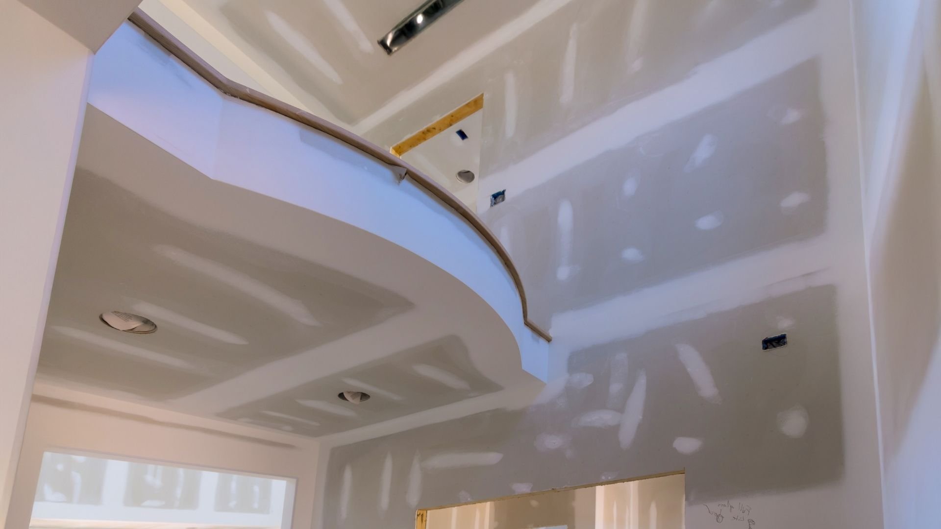 Interior ceiling under renovation with drywall, skylight opening, and construction materials visible.