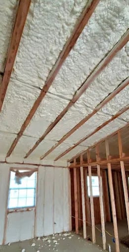 Interior construction with wooden ceiling joists and white insulation material installation.