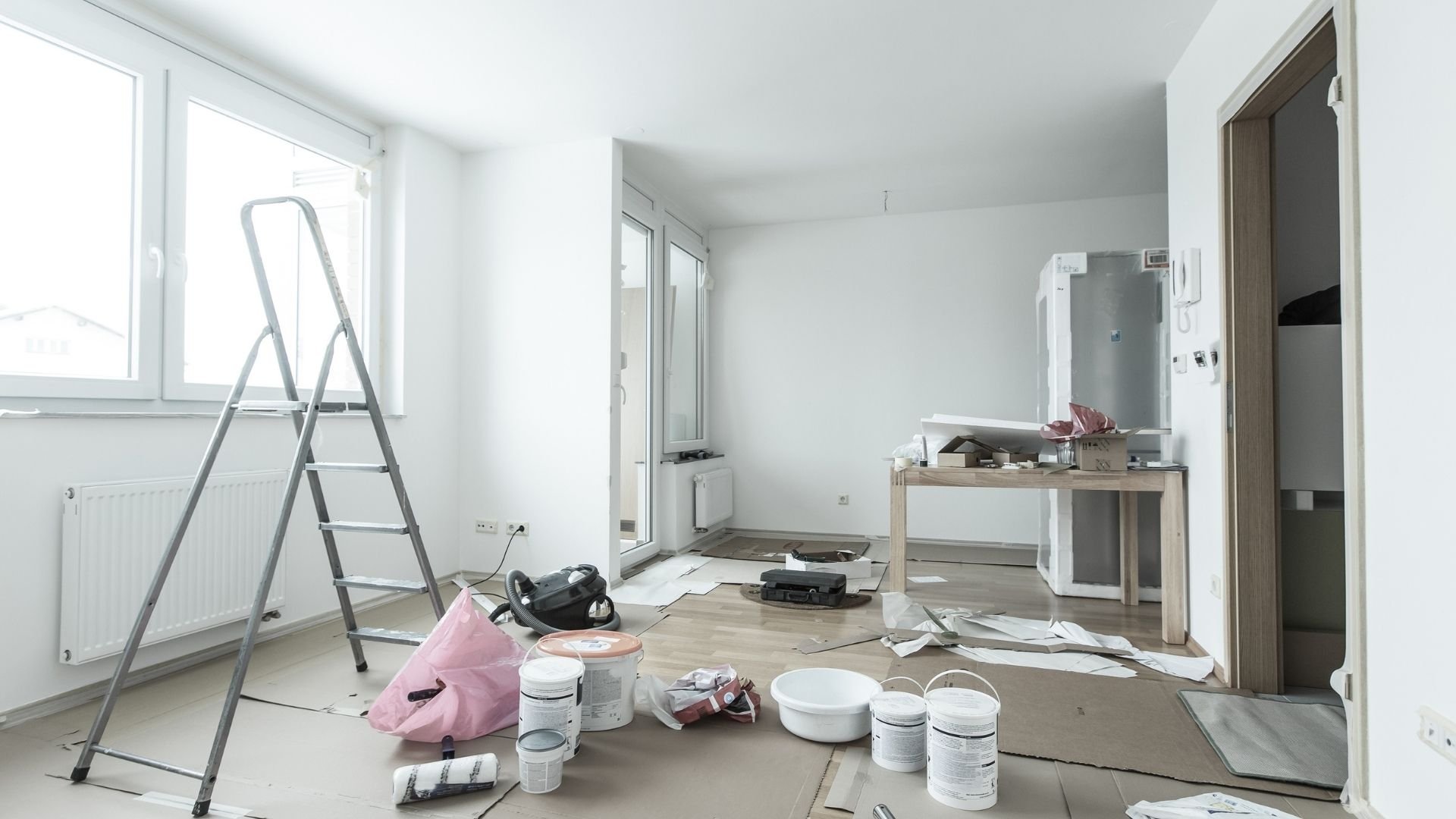 Unfinished apartment interior with ladder, paint supplies, and renovation materials scattered on floor