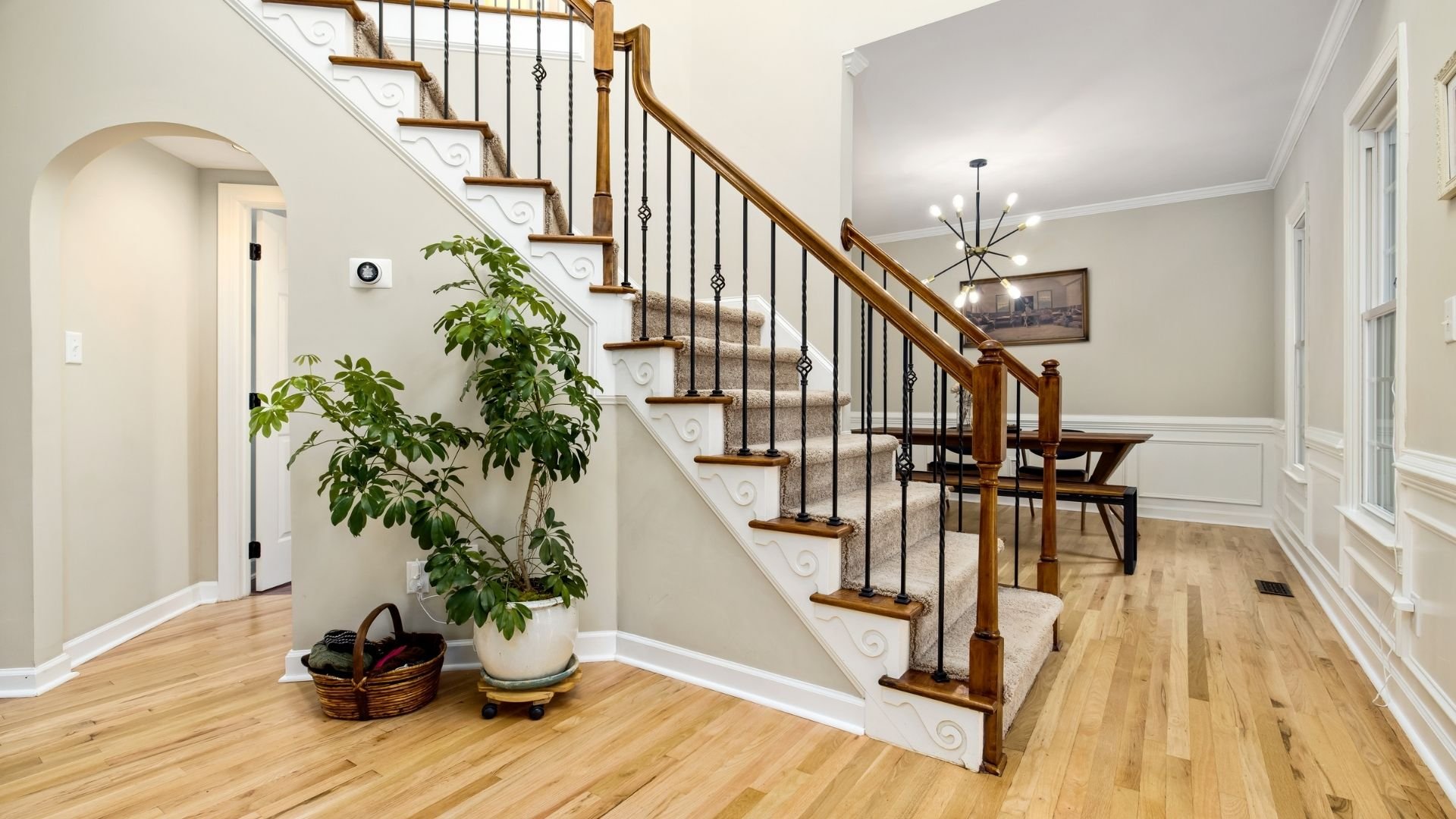 Modern foyer with wooden staircase, metal railings, hardwood floors, and green plant decor.